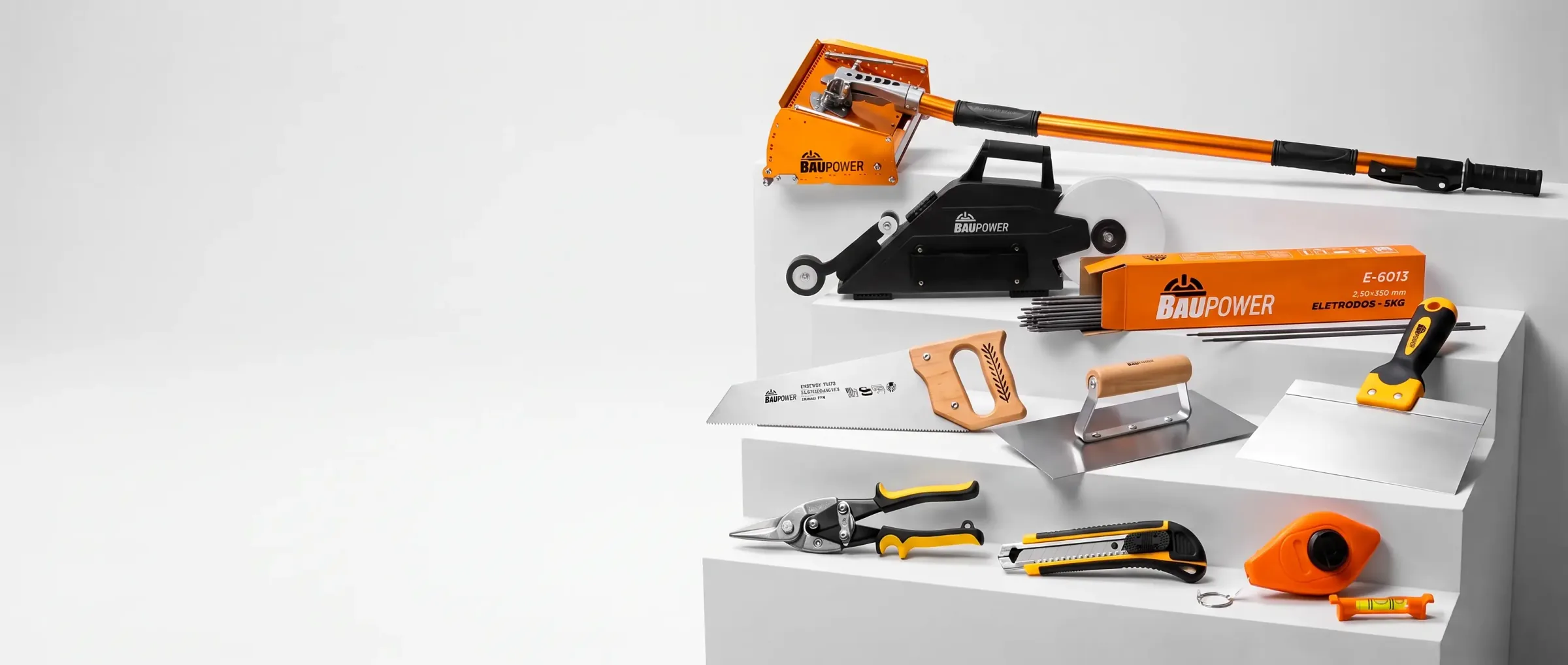 Linha Baupower disposta sobre degraus de estúdio: Flat Box, banjo aplicador de fita, caixa de eletrodos E-6013, serrote, desempenadeira, tesoura de perfil, estilete e nível