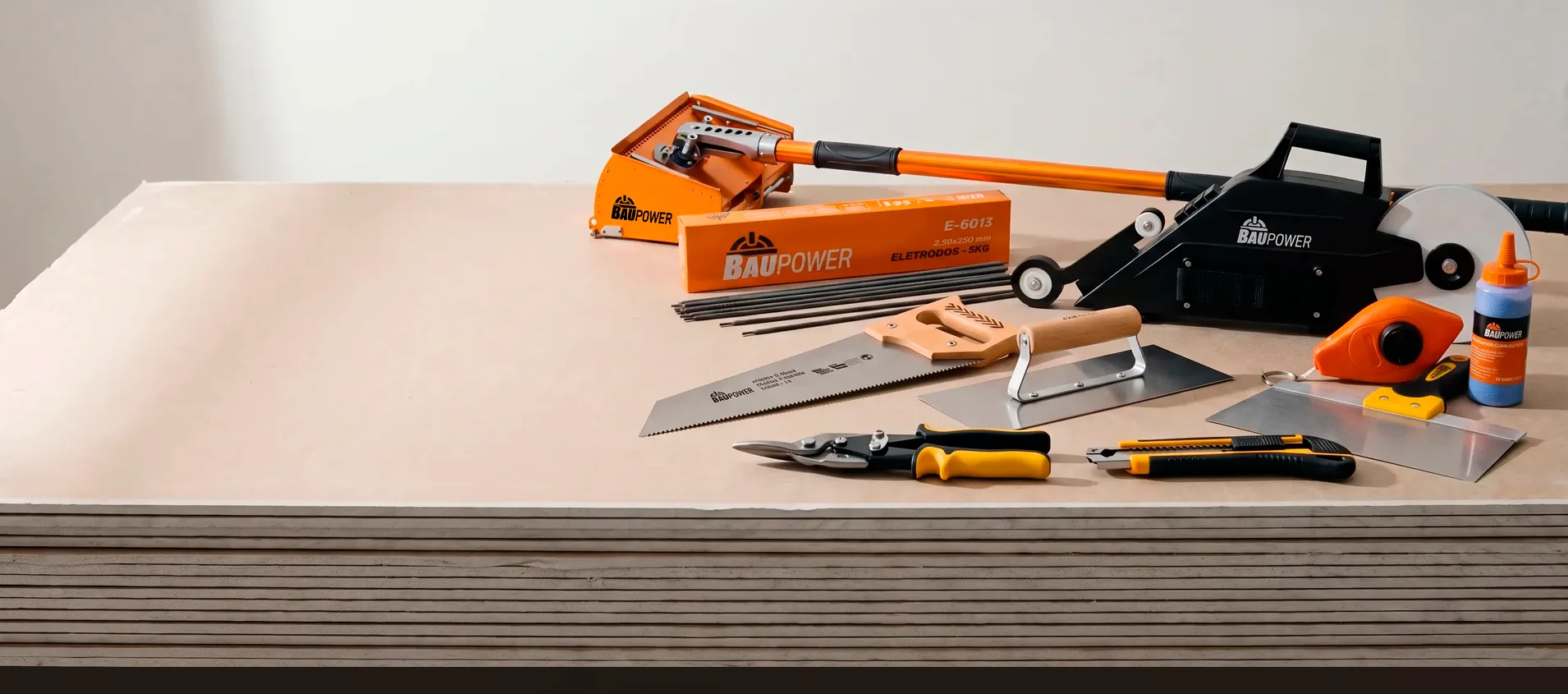 Linha drywall Baupower sobre uma pilha de placas de gesso: Flat Box, banjo aplicador de fita, caixa de eletrodos, serrote, desempenadeira, tesoura de perfil, estilete e giz de linha